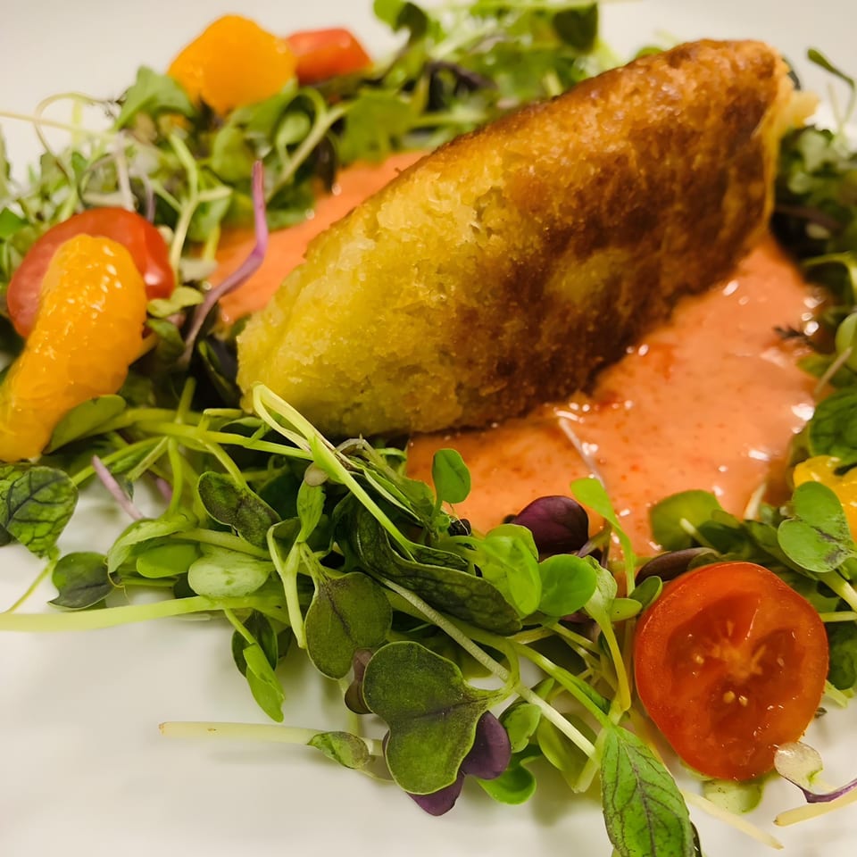 Crispy fried Thai dish on a bed of microgreens with cherry tomatoes and orange segments.