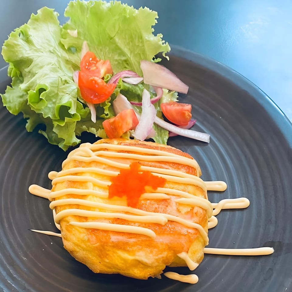 Thai Den's omelet with mayonnaise, orange roe, and a side salad on a dark plate.