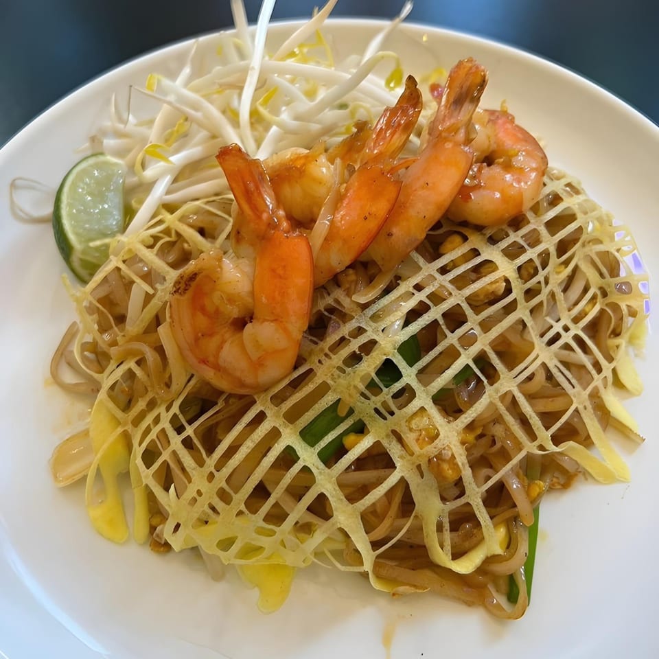Thai Den's Pad Thai with shrimp, bean sprouts, and a lime wedge, topped with an egg net.