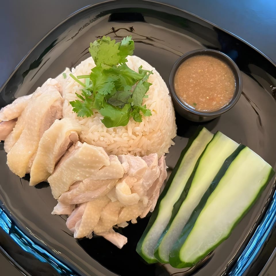 Thai Den's Khao Man Gai, with sliced chicken, rice, cilantro, cucumber, and dipping sauce.
