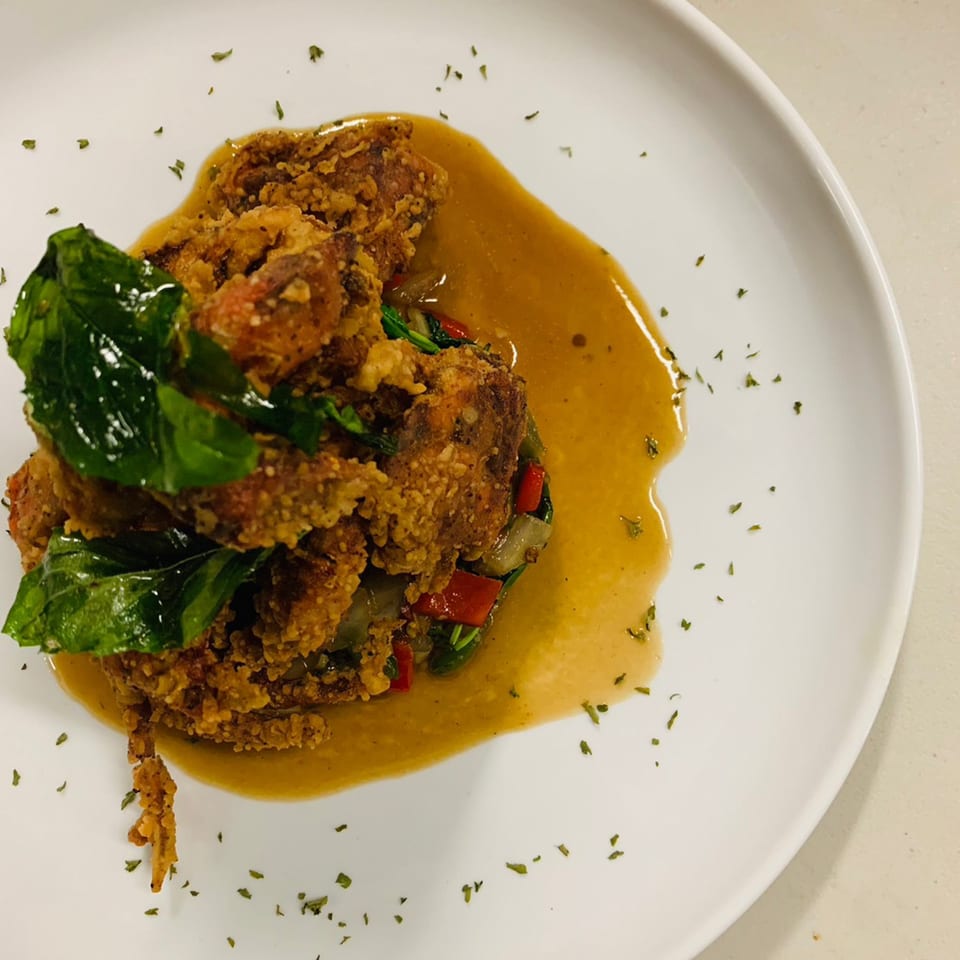Crispy fried soft-shell crab with basil leaves and a savory sauce on a white plate.